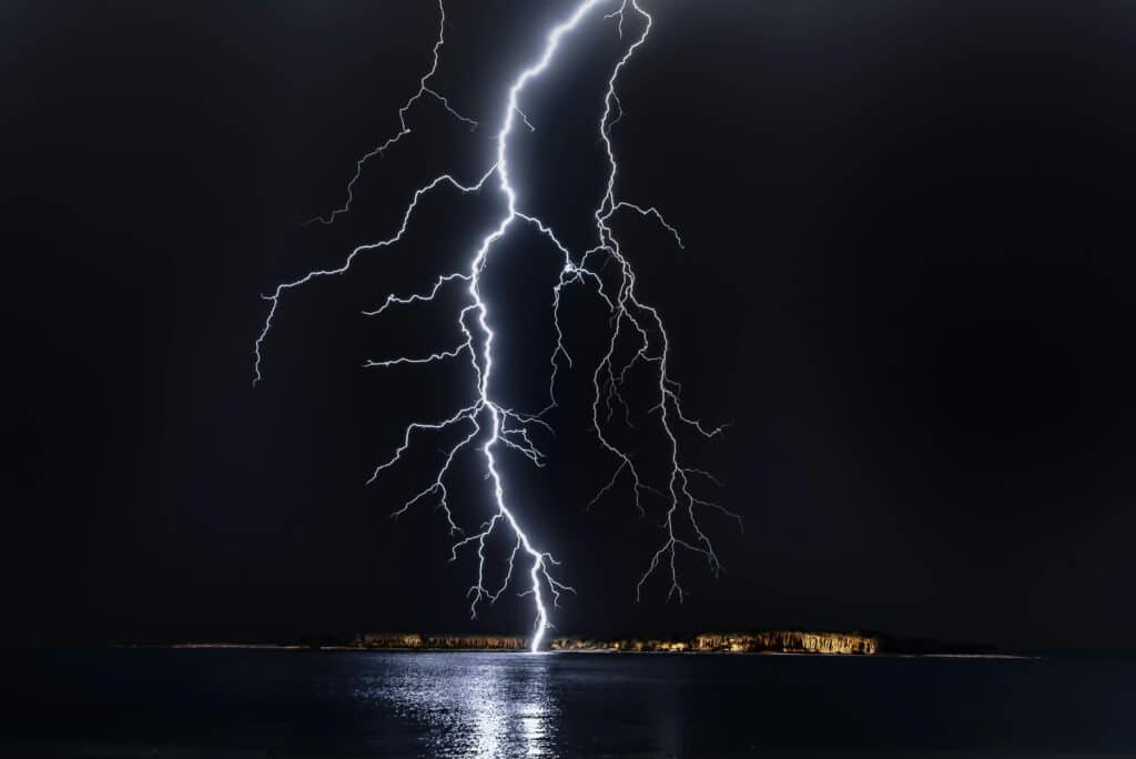 Dramatic lightning bolt over the ocean at night, illuminating the coastal landscape.