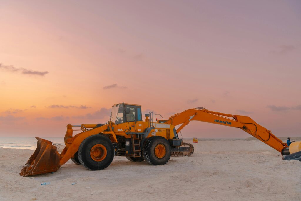 Excavator and bulldozer on a beach construction site during sunset.