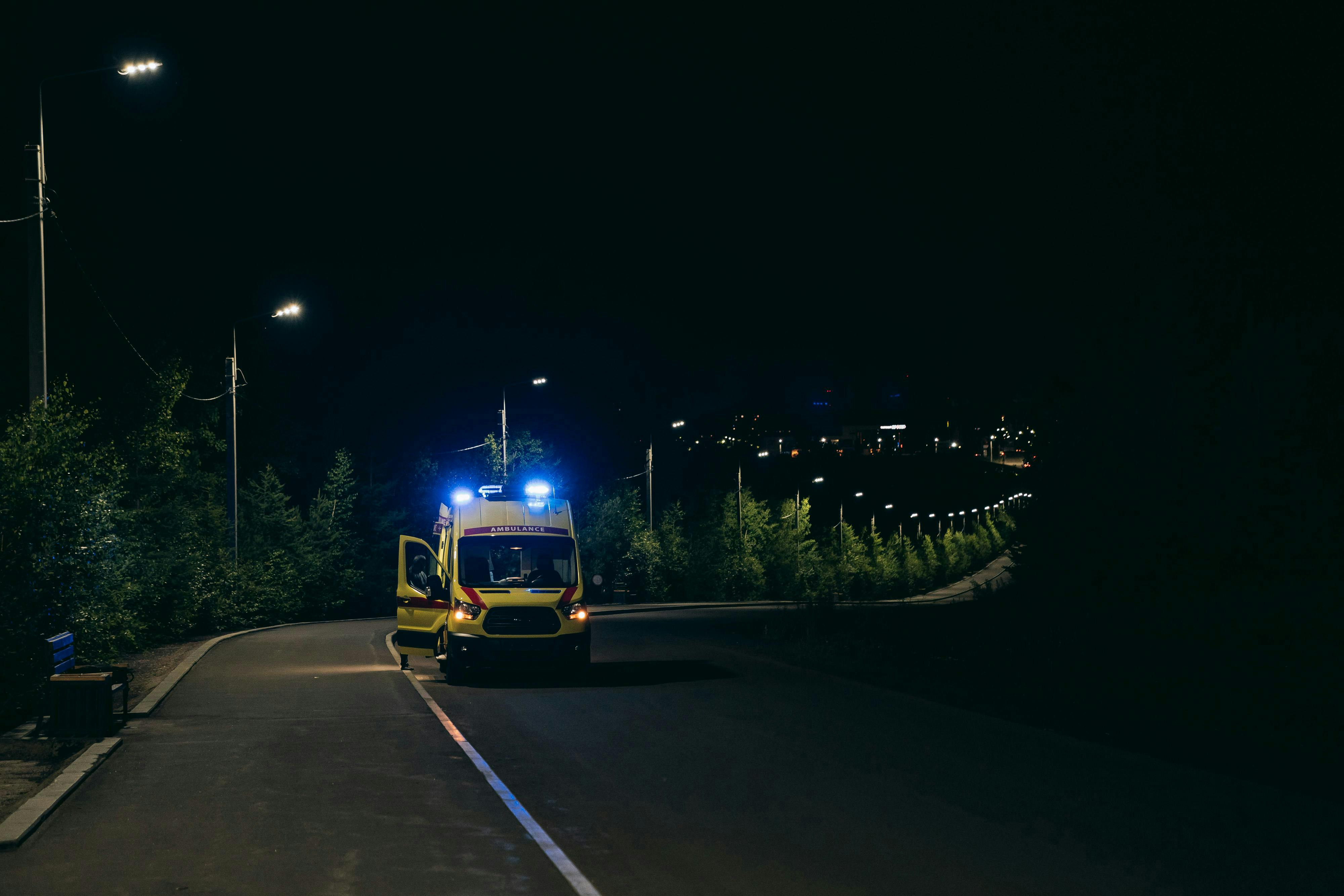 Ambulance with flashing lights on a rural road at night, ready for emergency response.