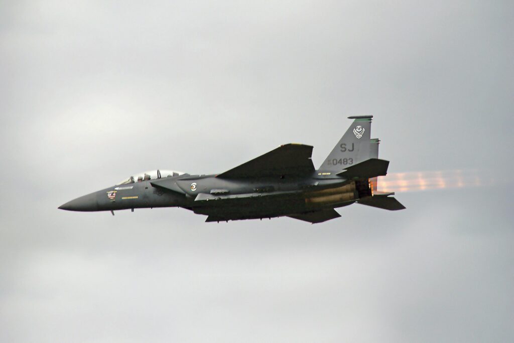 Dramatic view of F-15 fighter jet flying outdoors, showcasing afterburners against a cloudy sky.
