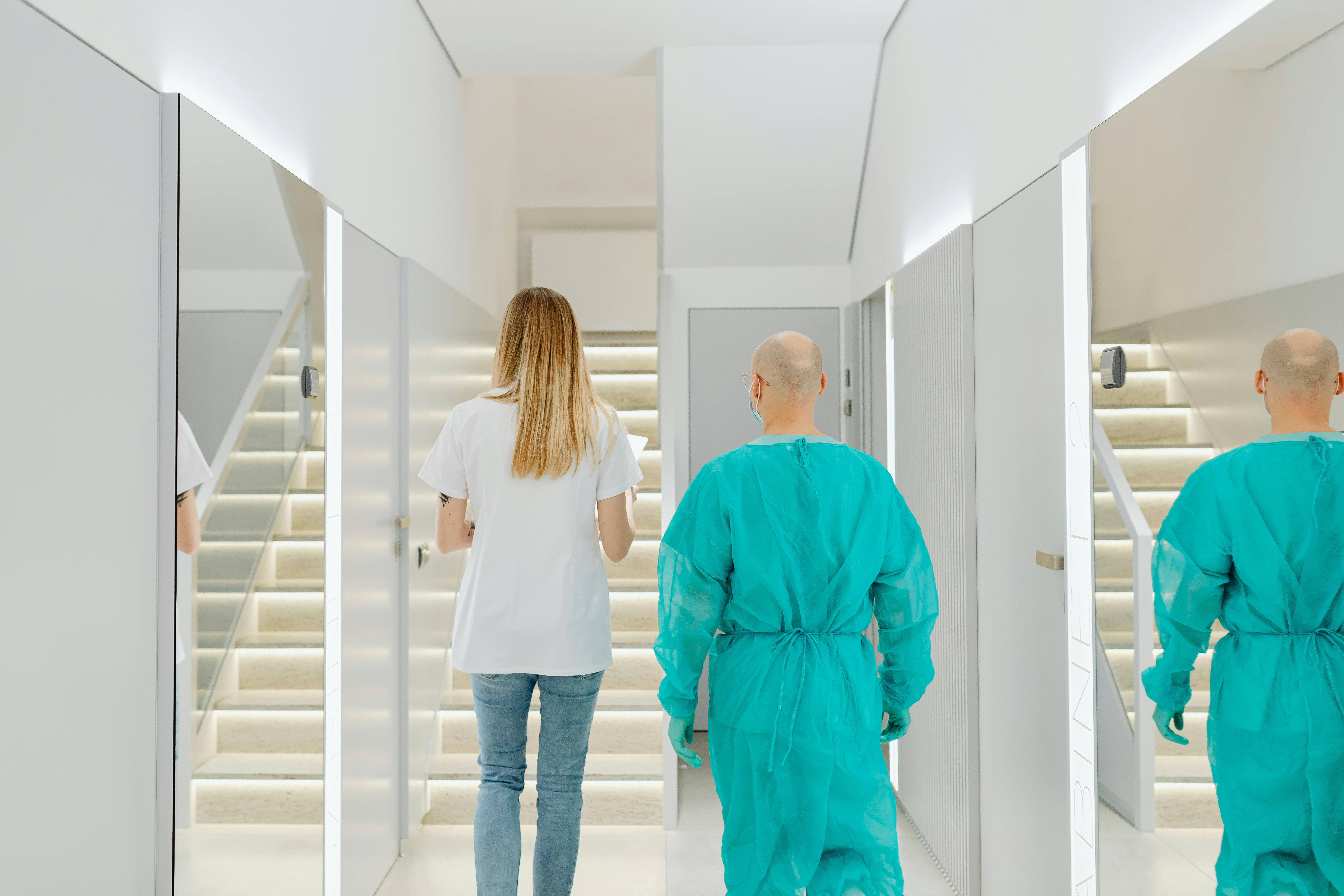 Two medical practitioners walking down a bright clinic hallway with reflections in mirrors.