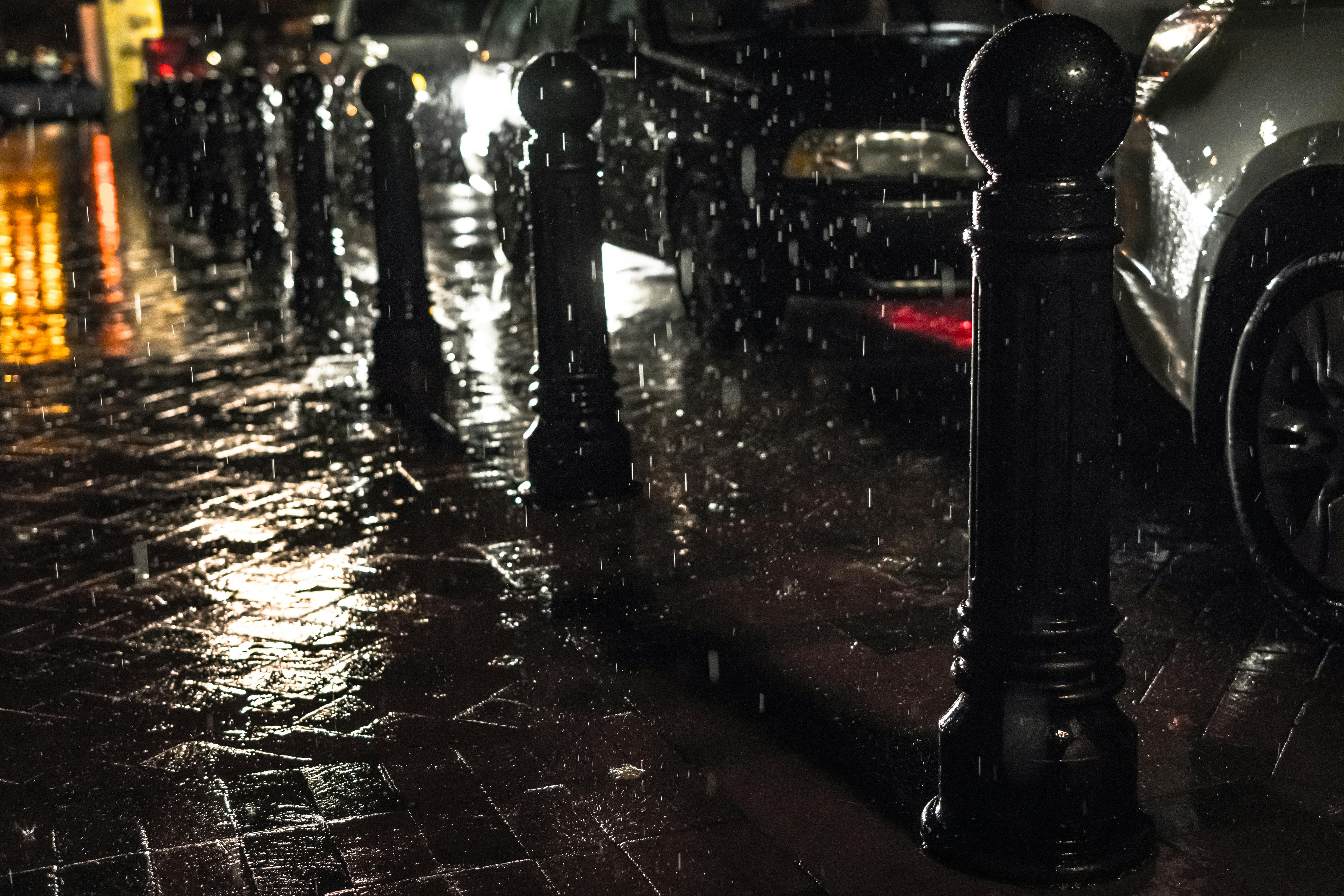 Urban street scene at night with rain and glistening pavement reflecting city lights.