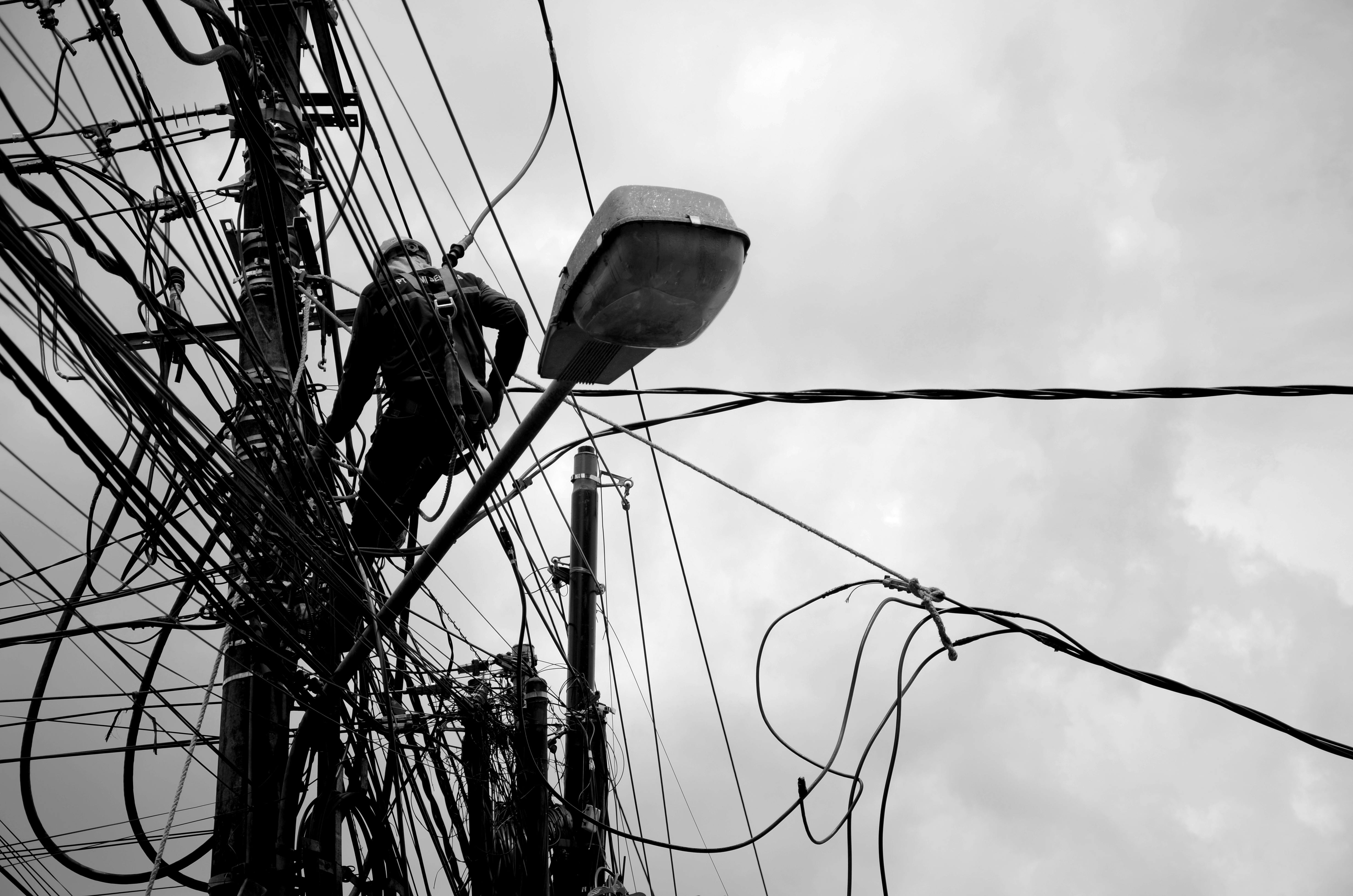 Black and white image of a technician working on power lines, illustrating electrical repair work.