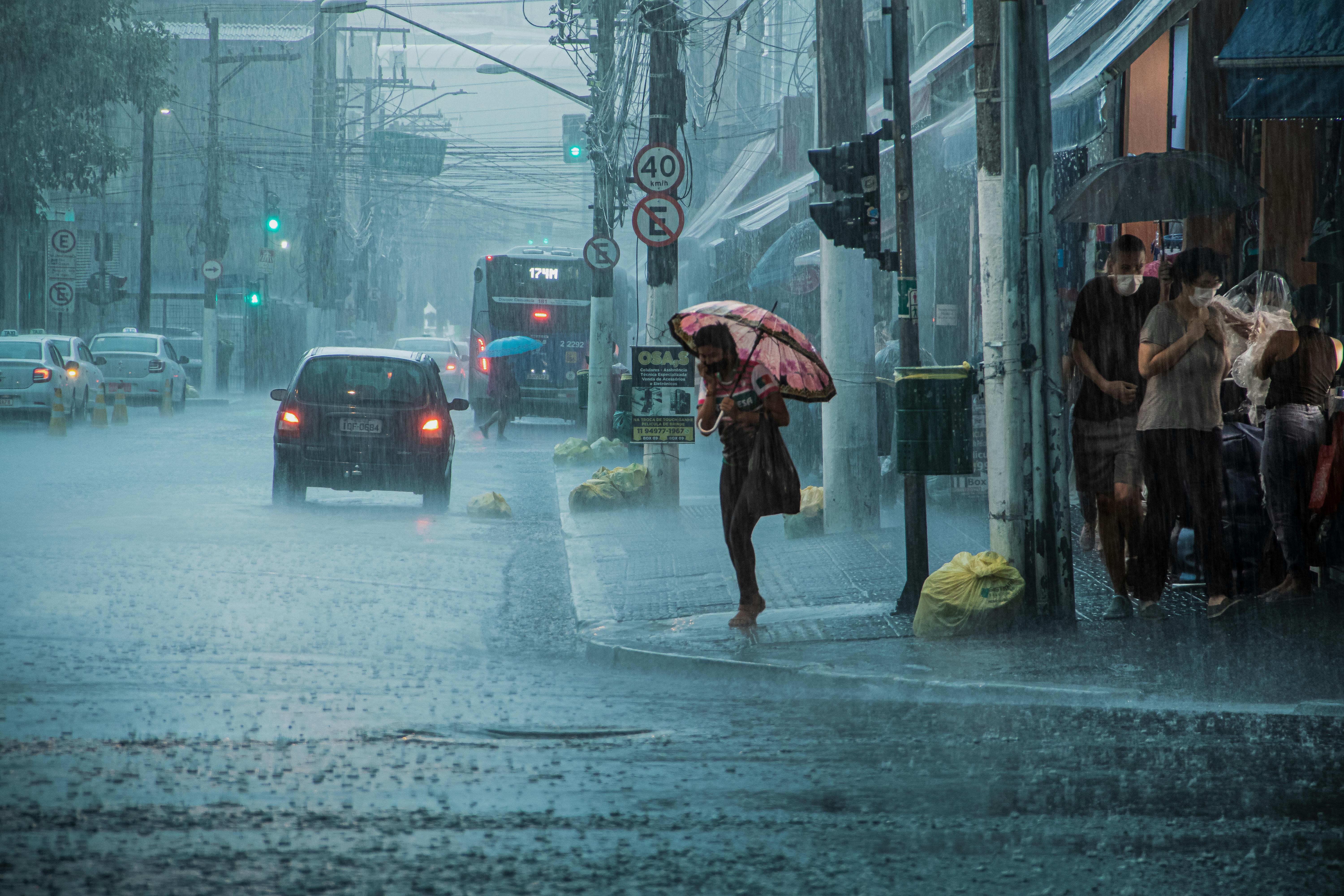 A busy urban street during heavy rain, with cars, pedestrians, and umbrellas.