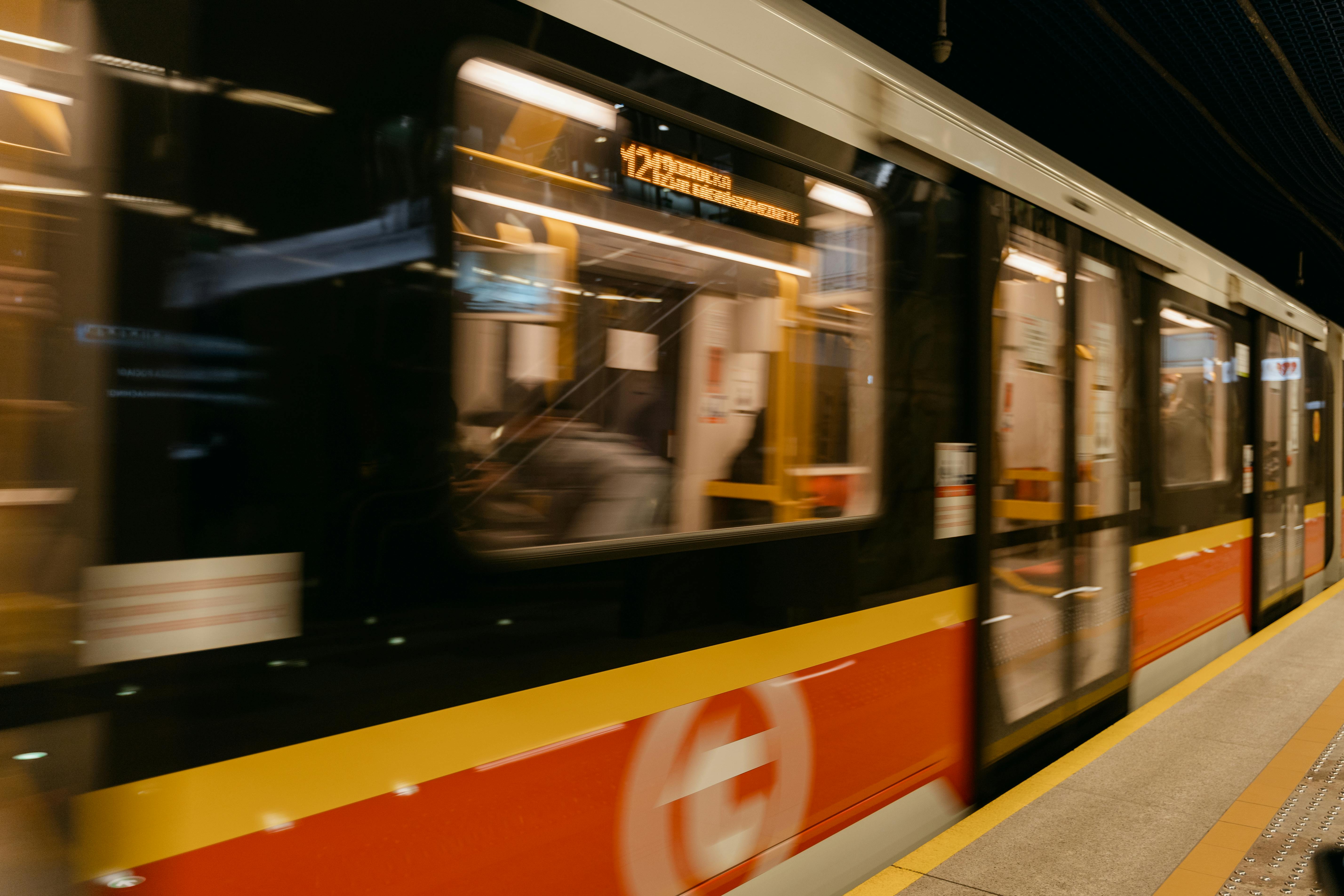 A blurred metro train speeds through an underground station with passengers on board.
