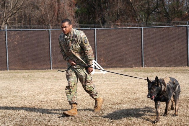 Military Working Dog Nick sits with his handler, Staff Sgt. Justin Peyton, during his retirement ceremony at Fort George G. Meade, Md., Jan. 21, 2024. After eight years of decorated service, Nick will retire to the Peyton family home. (U.S. Army photo)