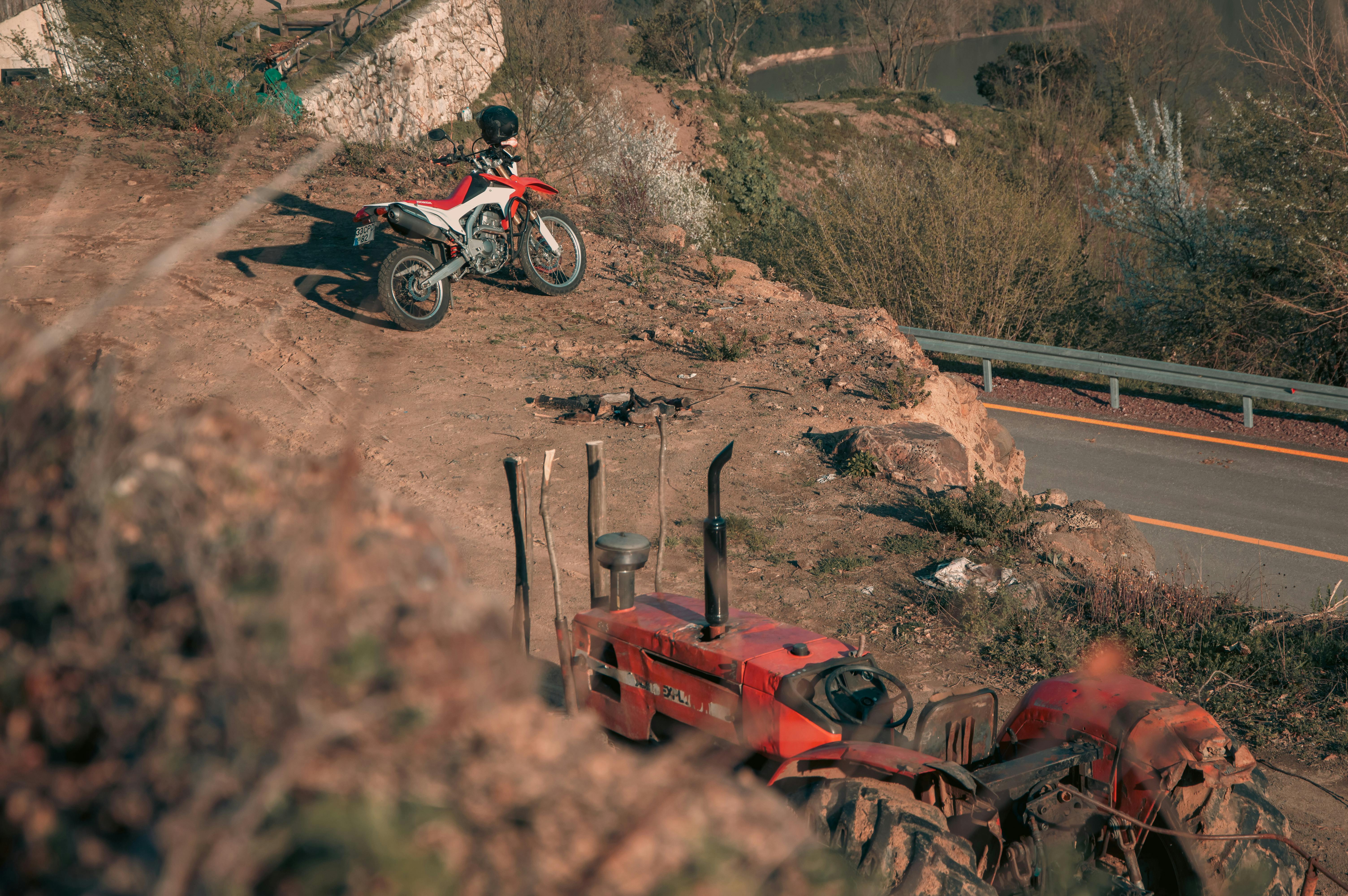 A motorbike and tractor parked on a rocky hill with a road visible in the background.