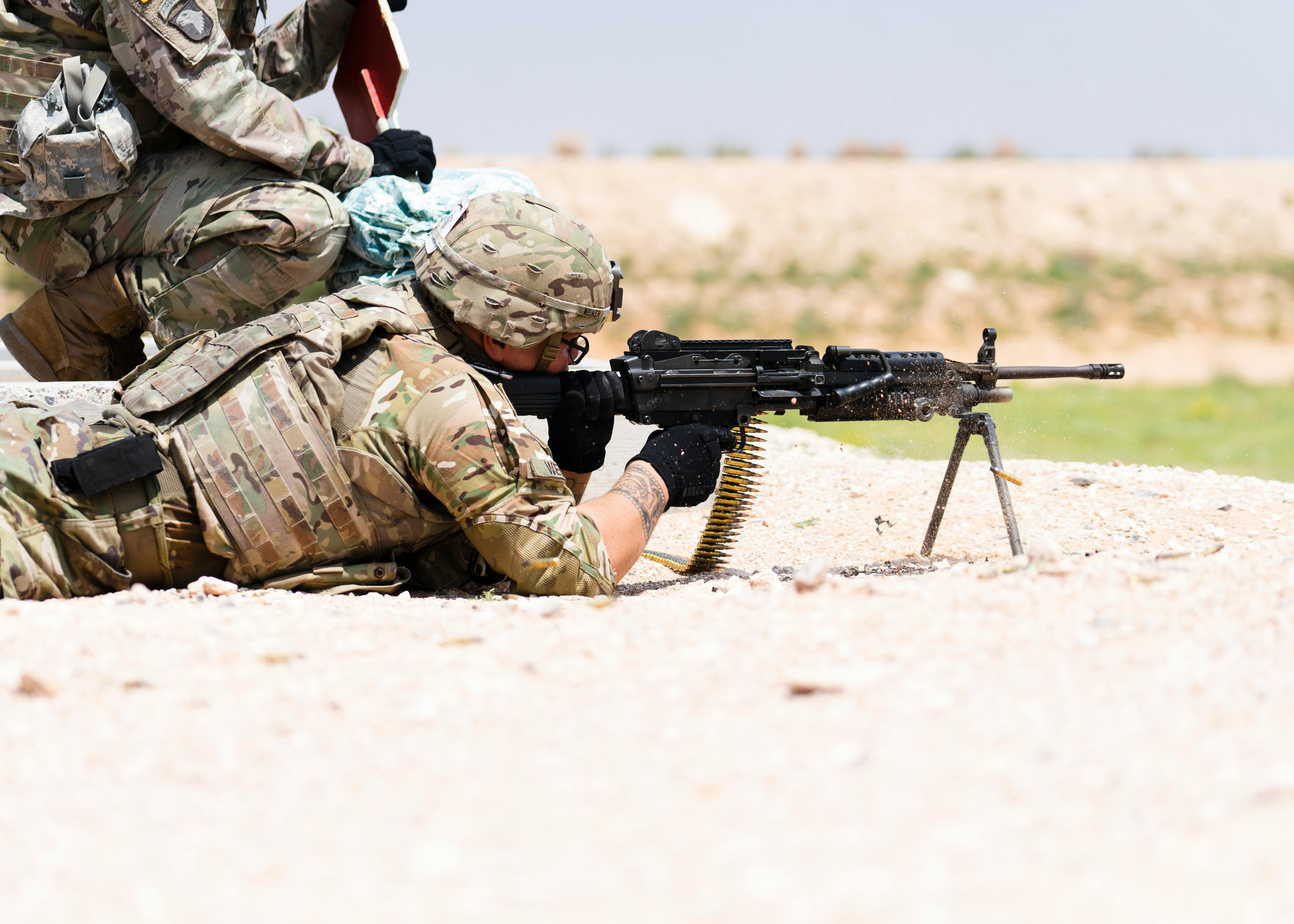 US soldier in camouflage uniform using a machine gun in outdoor military training.