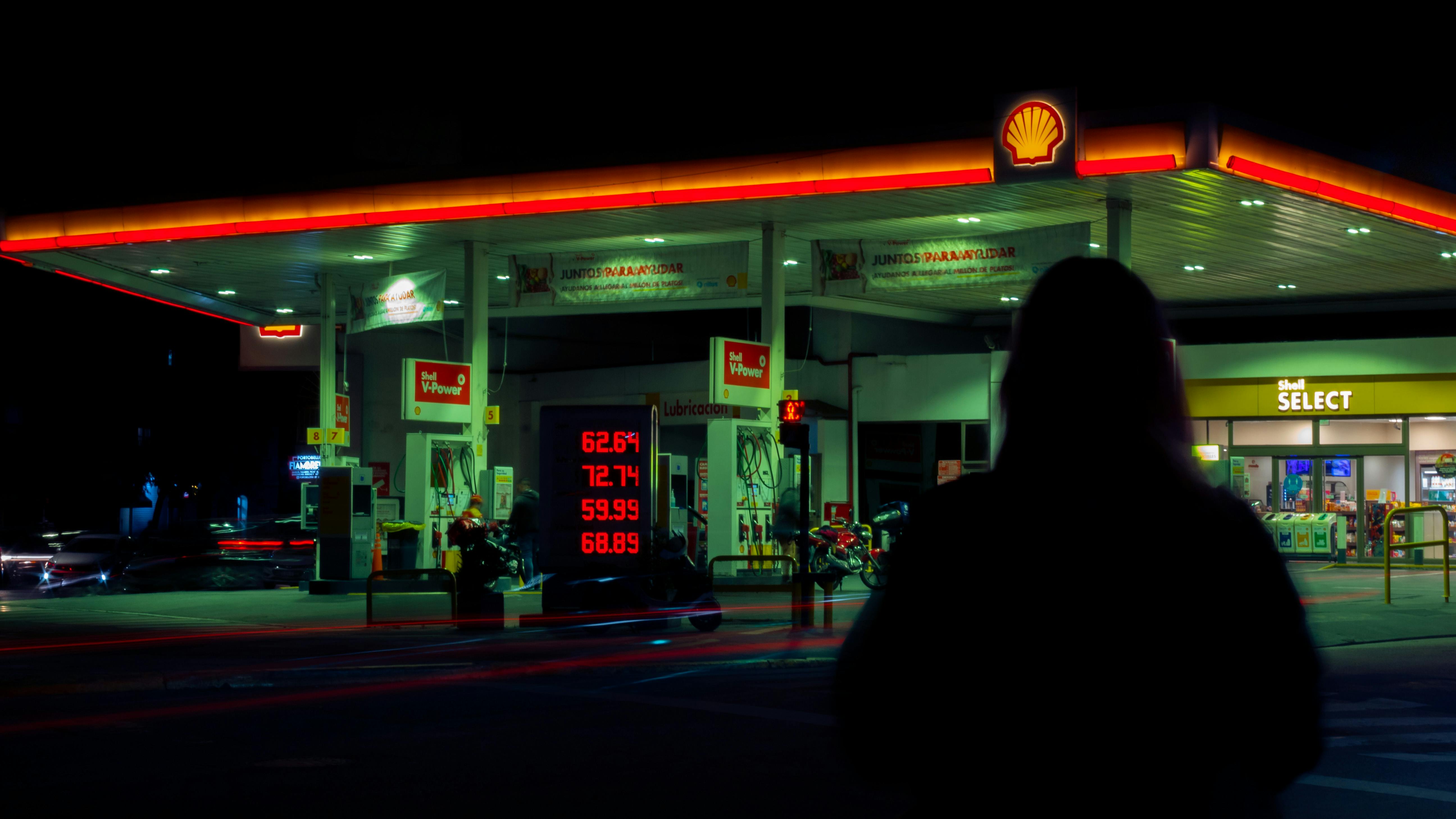 A petrol station illuminated at night with a person's silhouette in foreground, capturing urban ambiance.