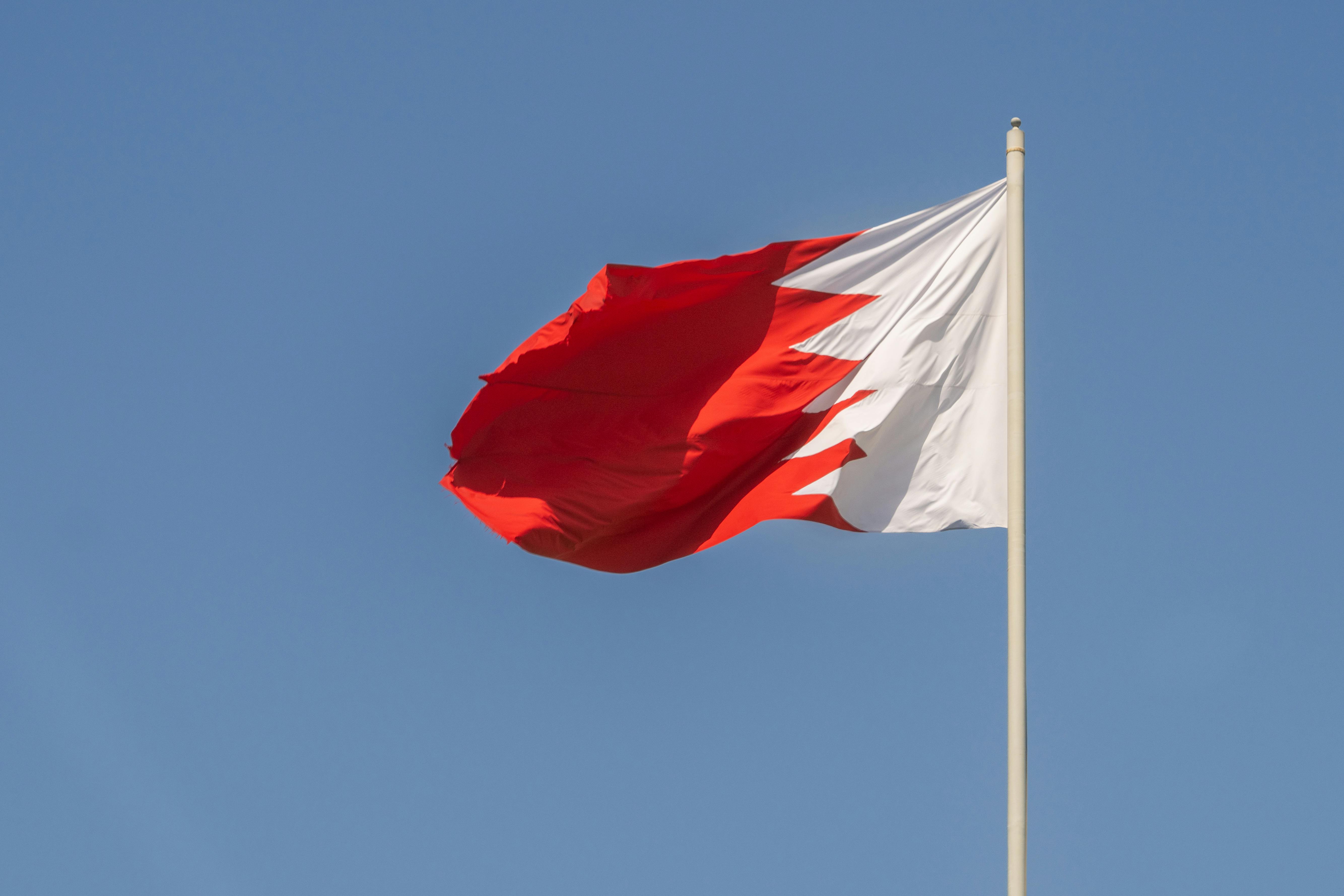 Bahraini national flag waving prominently against a clear blue sky, symbolizing national pride.