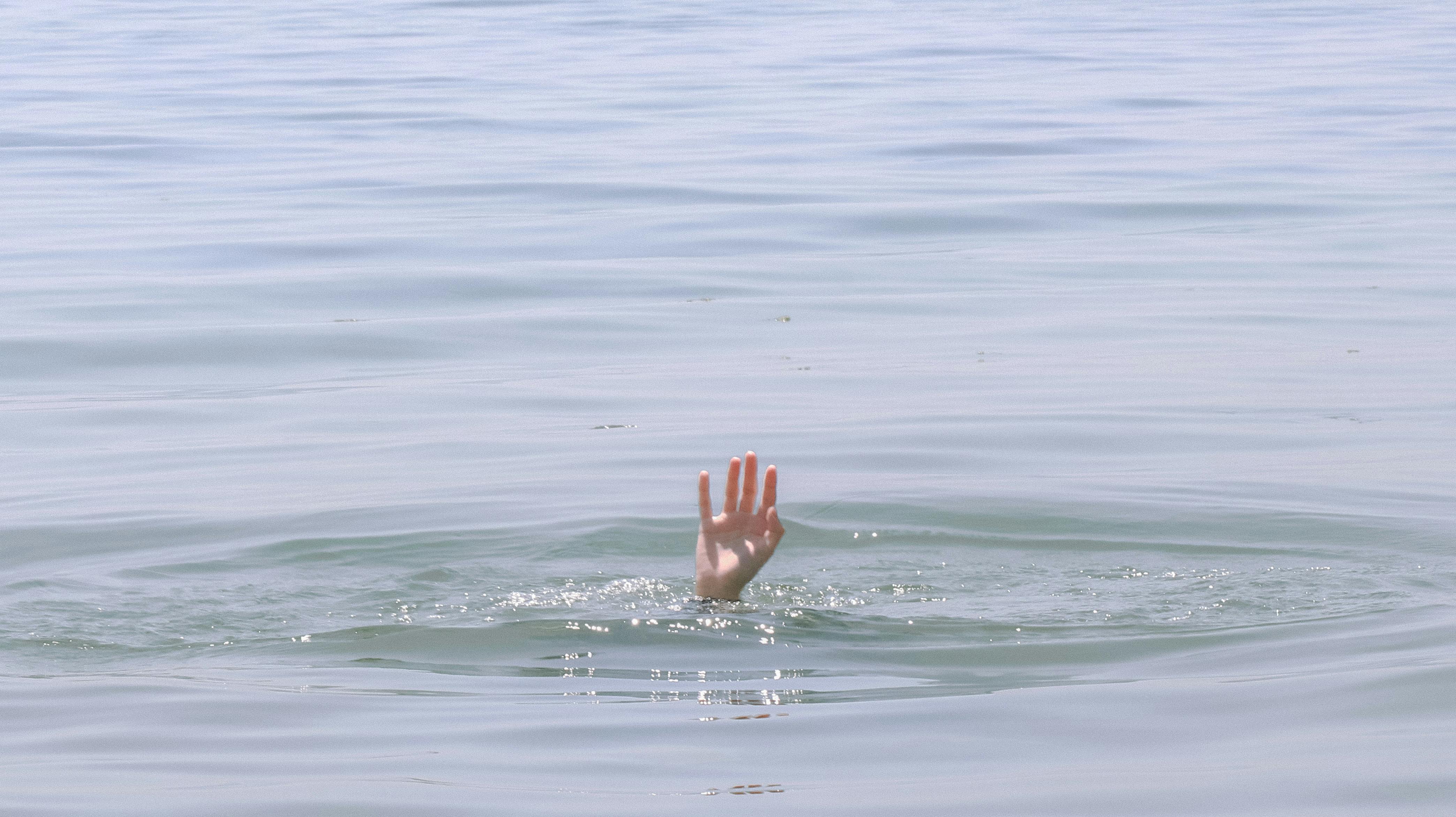 A hand reaching out of calm water on a sunny day, hinting at themes of rescue and serenity.