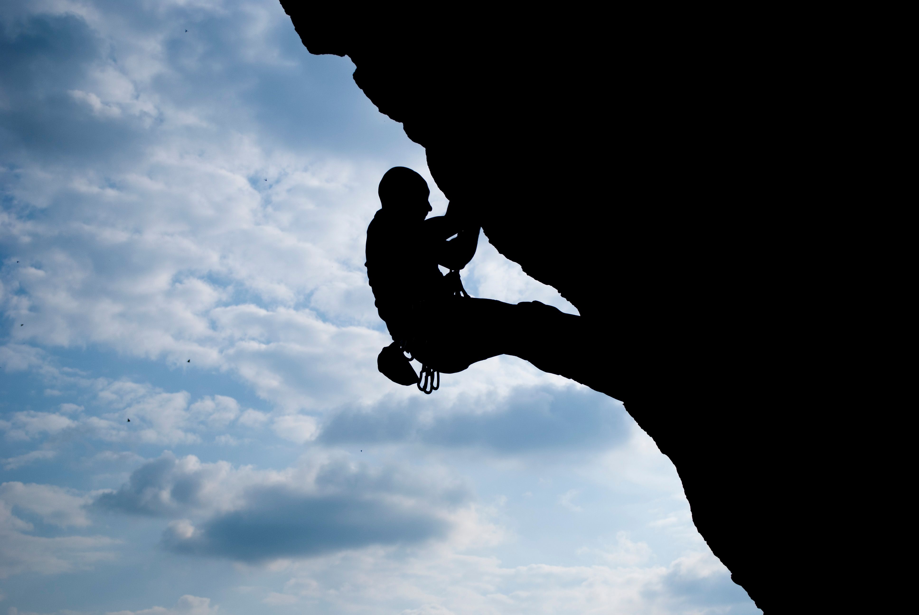 Dramatic silhouette of a solo rock climber against cloudy sky in Umbria, Italy.