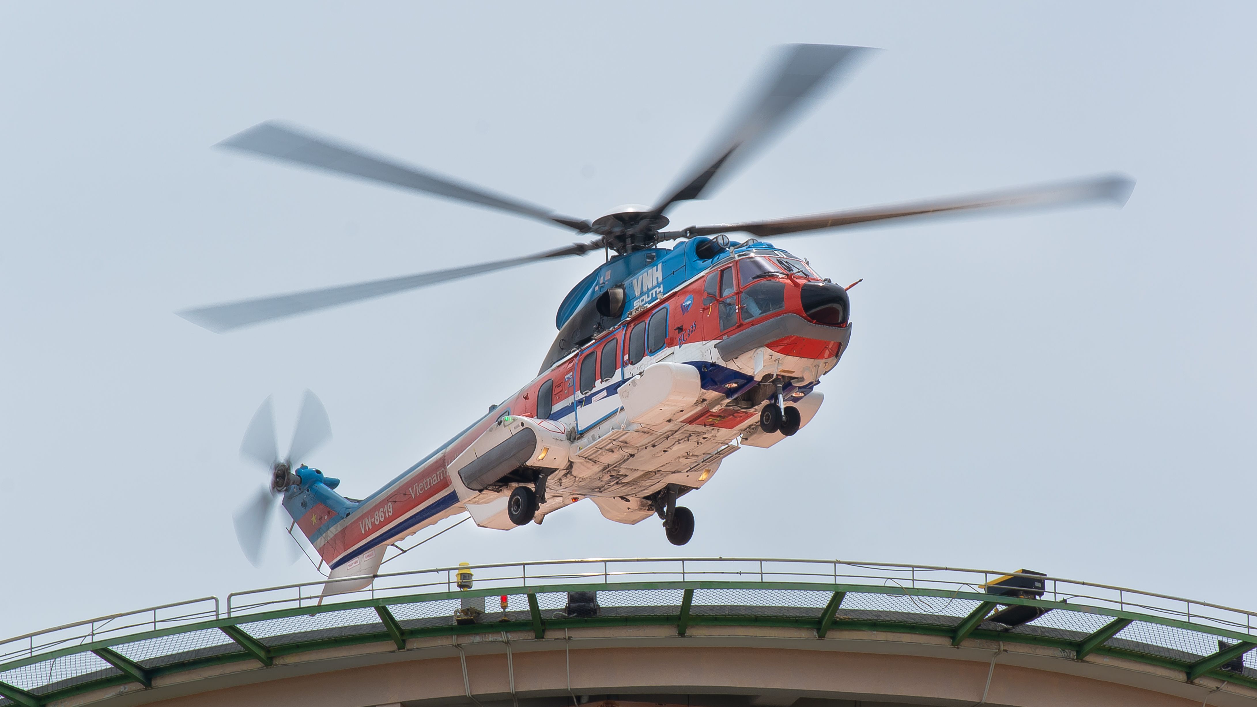 Dynamic shot of a helicopter landing on a rooftop helipad in an urban setting, showcasing aviation precision.