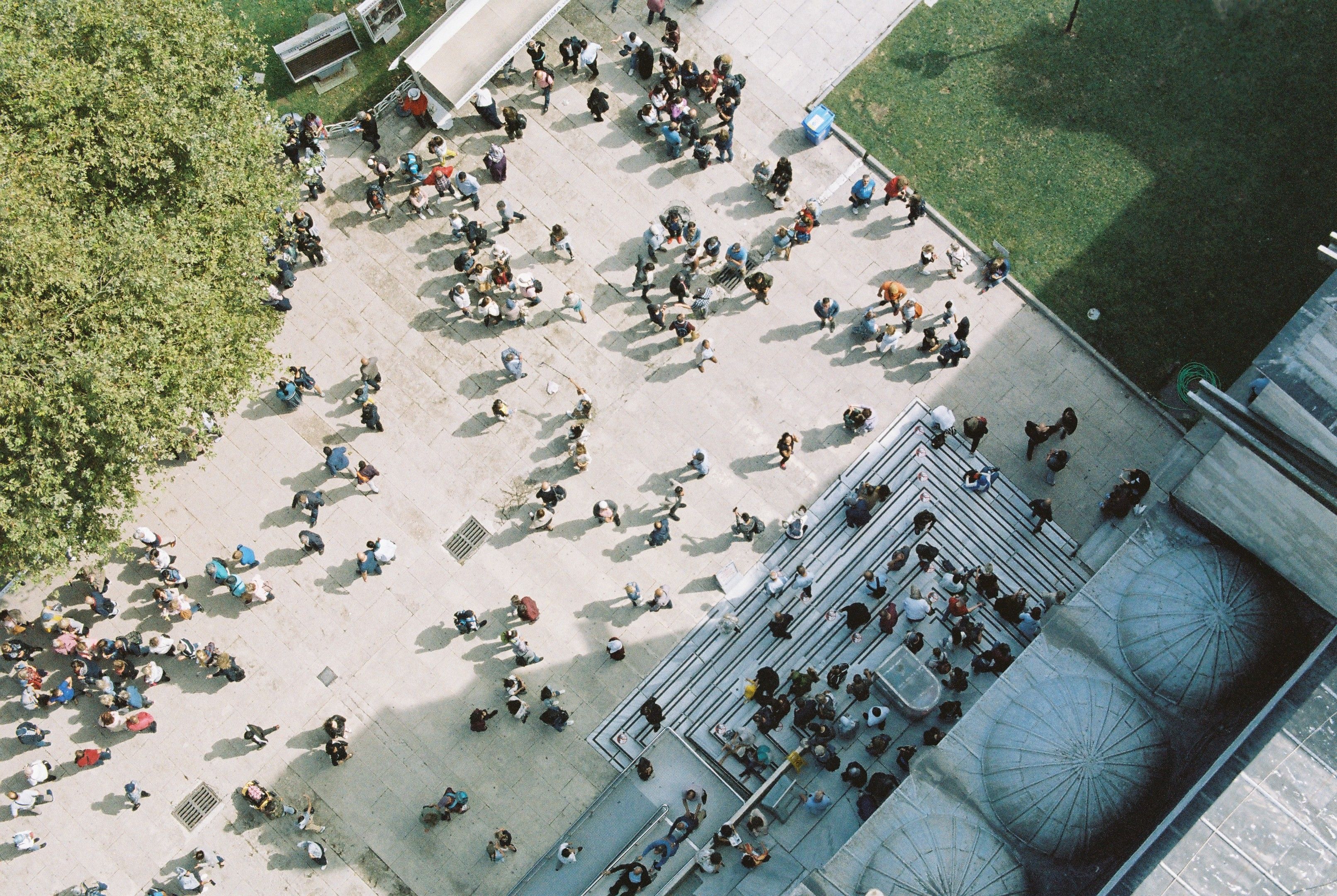 An aerial shot capturing a bustling city plaza filled with diverse crowds on a sunny day.